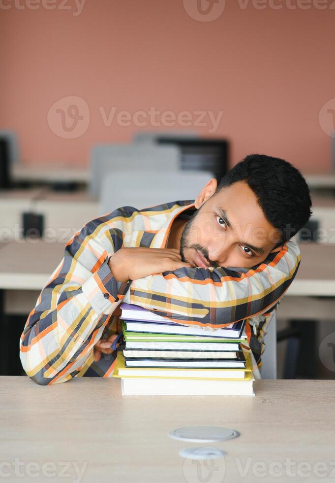 Young indian student boy reading book studying in college library with bookshelf behind. working on assignment or project photo