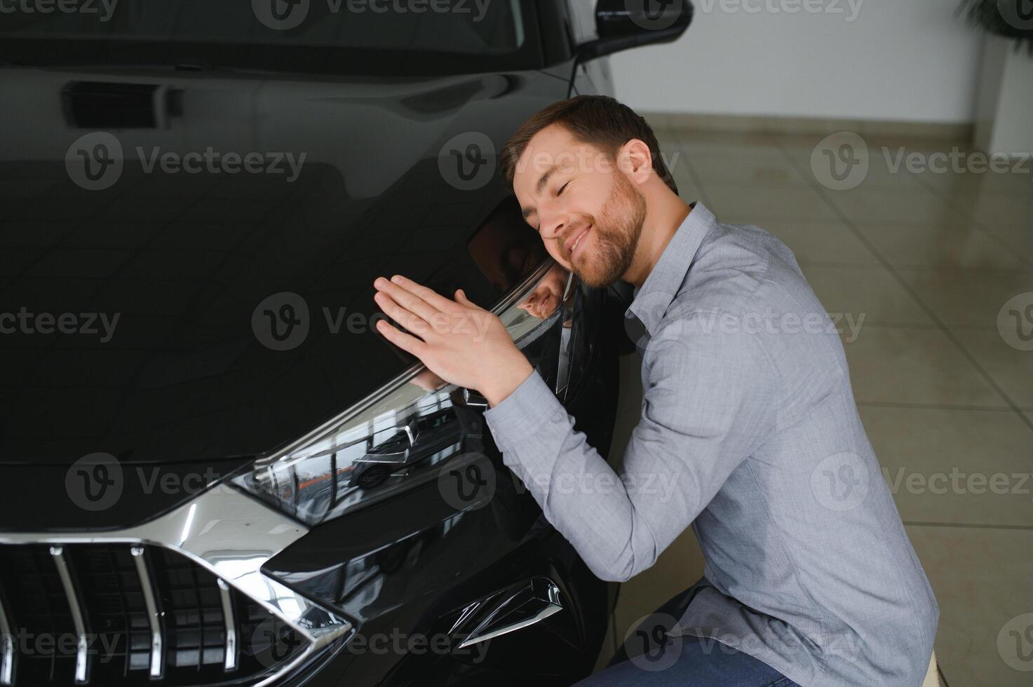 Visiting car dealership. Handsome bearded man is stroking his new car and smiling. photo