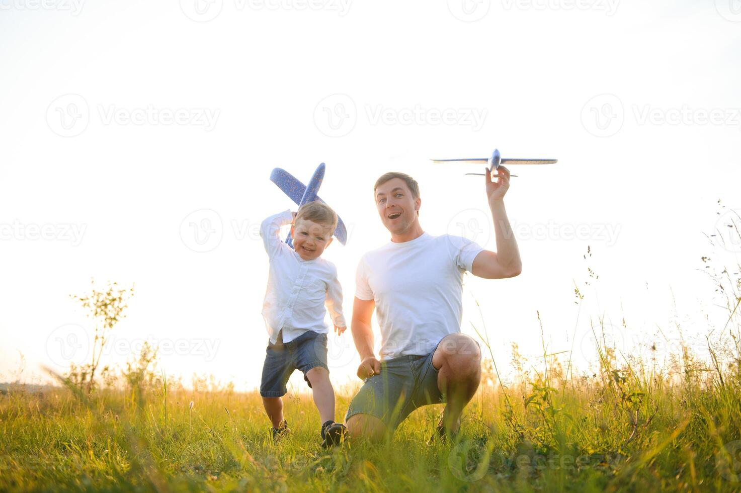 Happy father child moment. Father piggybacking his boy at sunset while he's playing with toy plane. photo