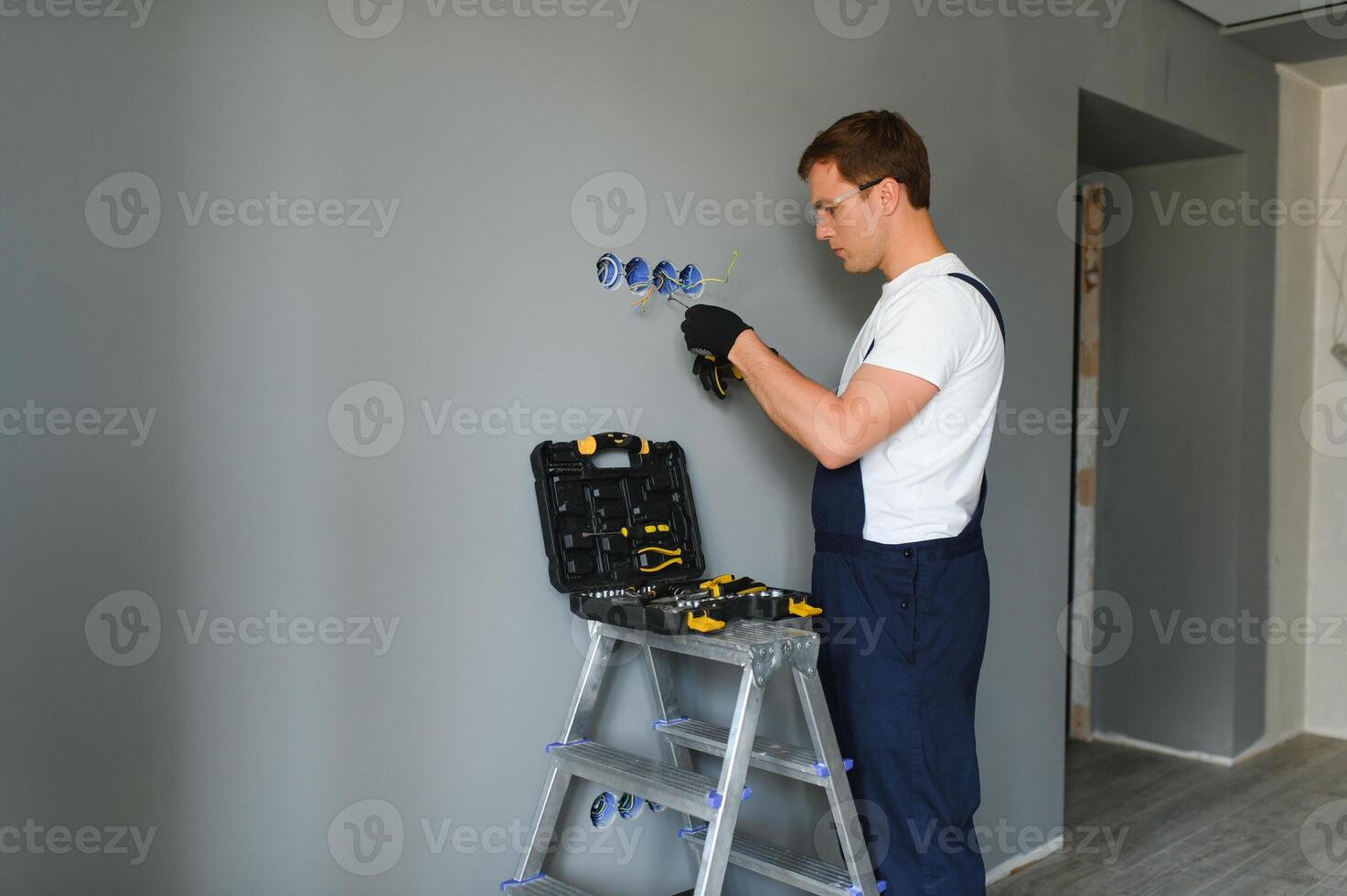 Electrician with screwdriver repairing power socket in room photo