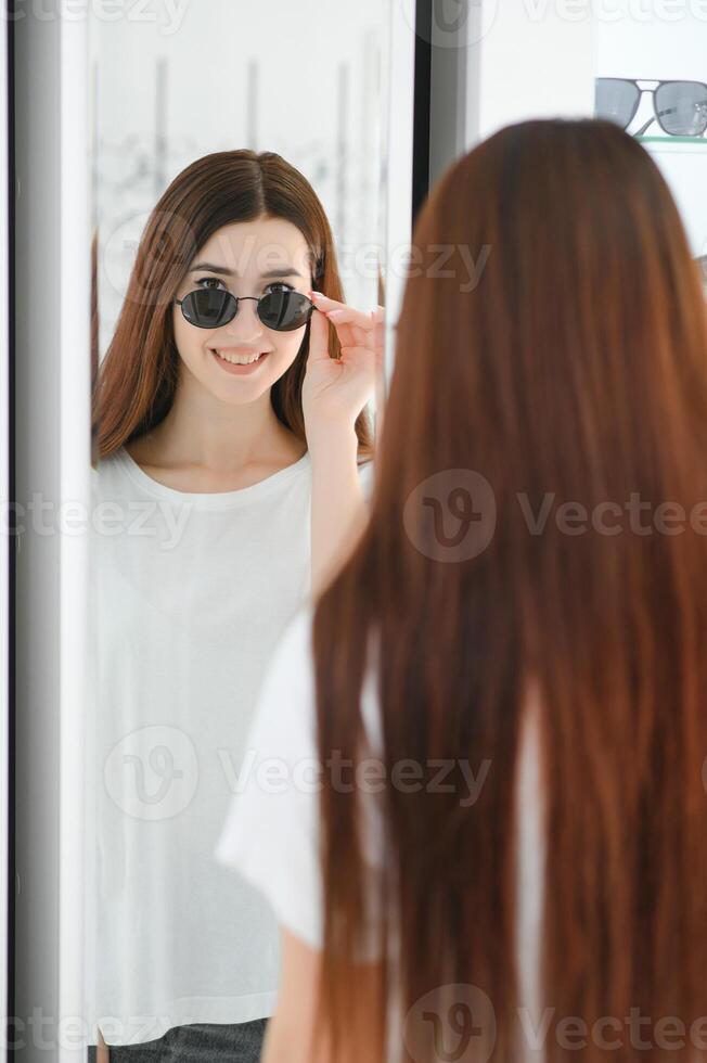 young woman chooses sunglasses for herself in an optics store photo