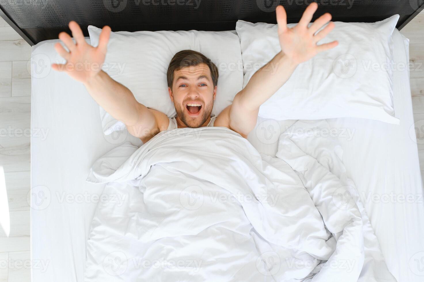 bueno Mañana. joven hombre despertar arriba en cama y extensión su brazos foto