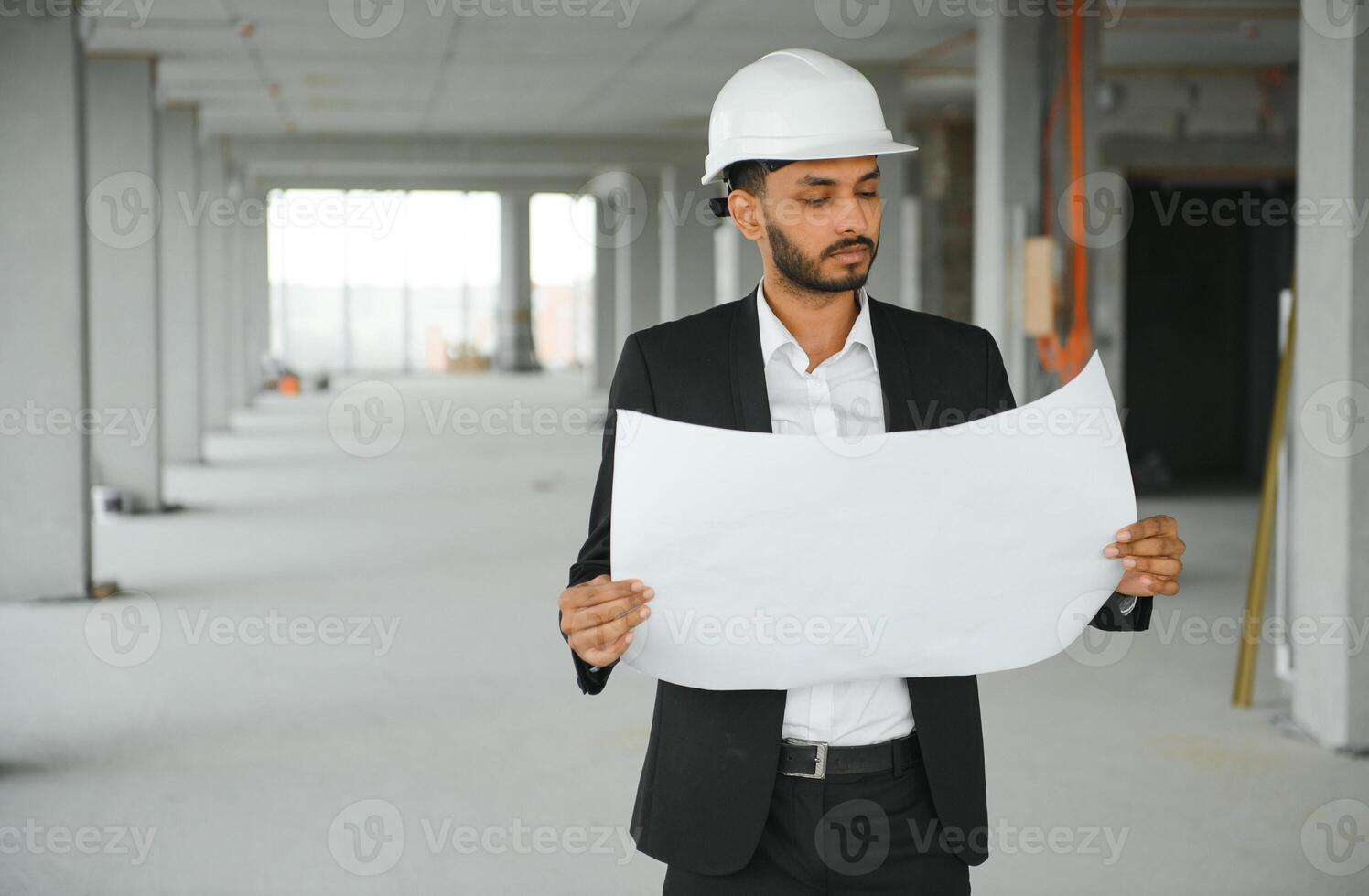 Indian construction site manager standing wearing helmet, thinking at construction site. Portrait of mixed race manual worker or architect. photo