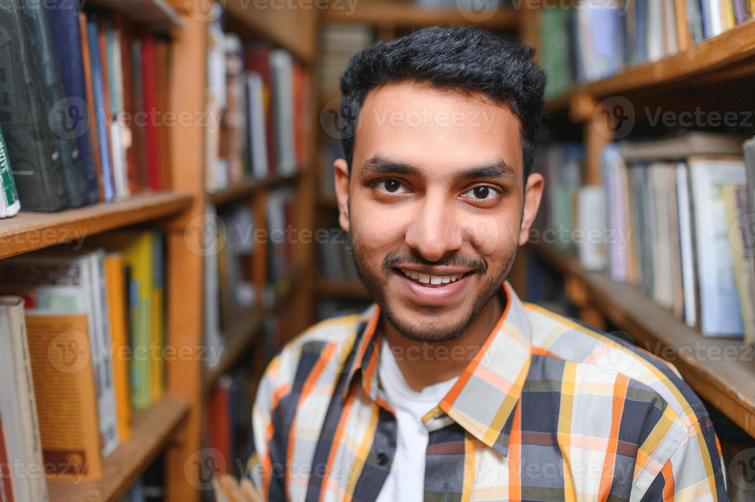 retrato de alegre masculino internacional indio estudiante con mochila, aprendizaje accesorios en pie cerca estantería a Universidad biblioteca o libro Tienda durante descanso Entre lecciones educación concepto foto