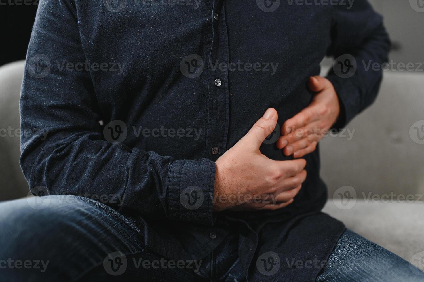Unhappy senior man stomach ache, man presses hand to stomach from unbearable pain, mature man with stomach pain feeling unwell sitting in living room photo