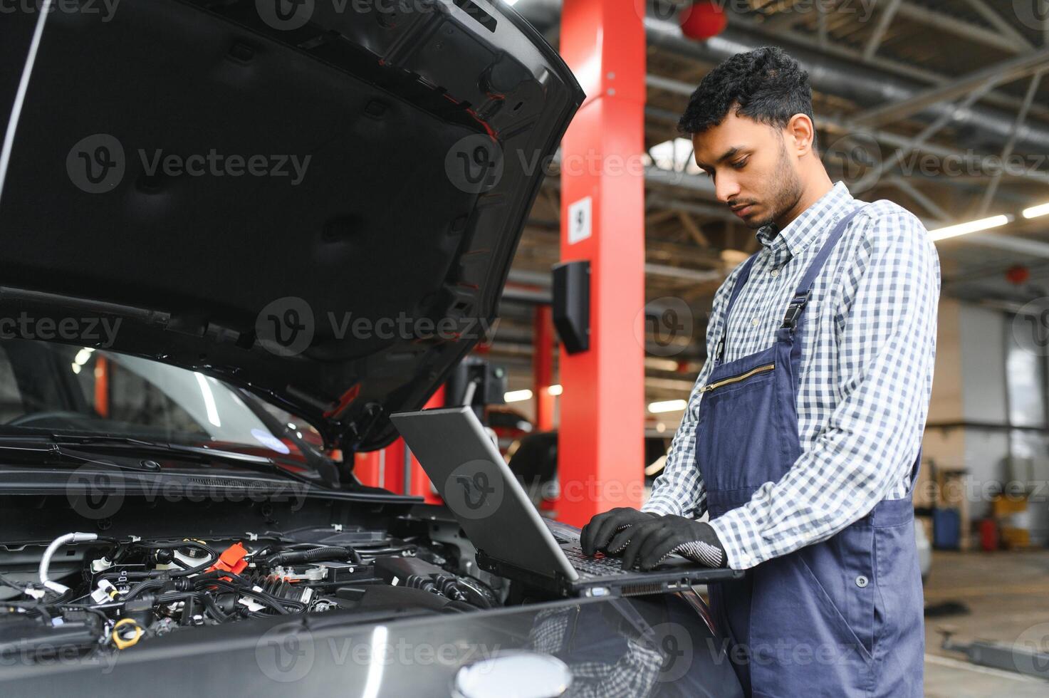 mecánico hombre mecánico gerente trabajador utilizando un ordenador portátil computadora comprobación coche en taller a auto coche reparar Servicio centro. ingeniero joven hombre mirando a inspección vehículo detalles debajo coche capucha. foto