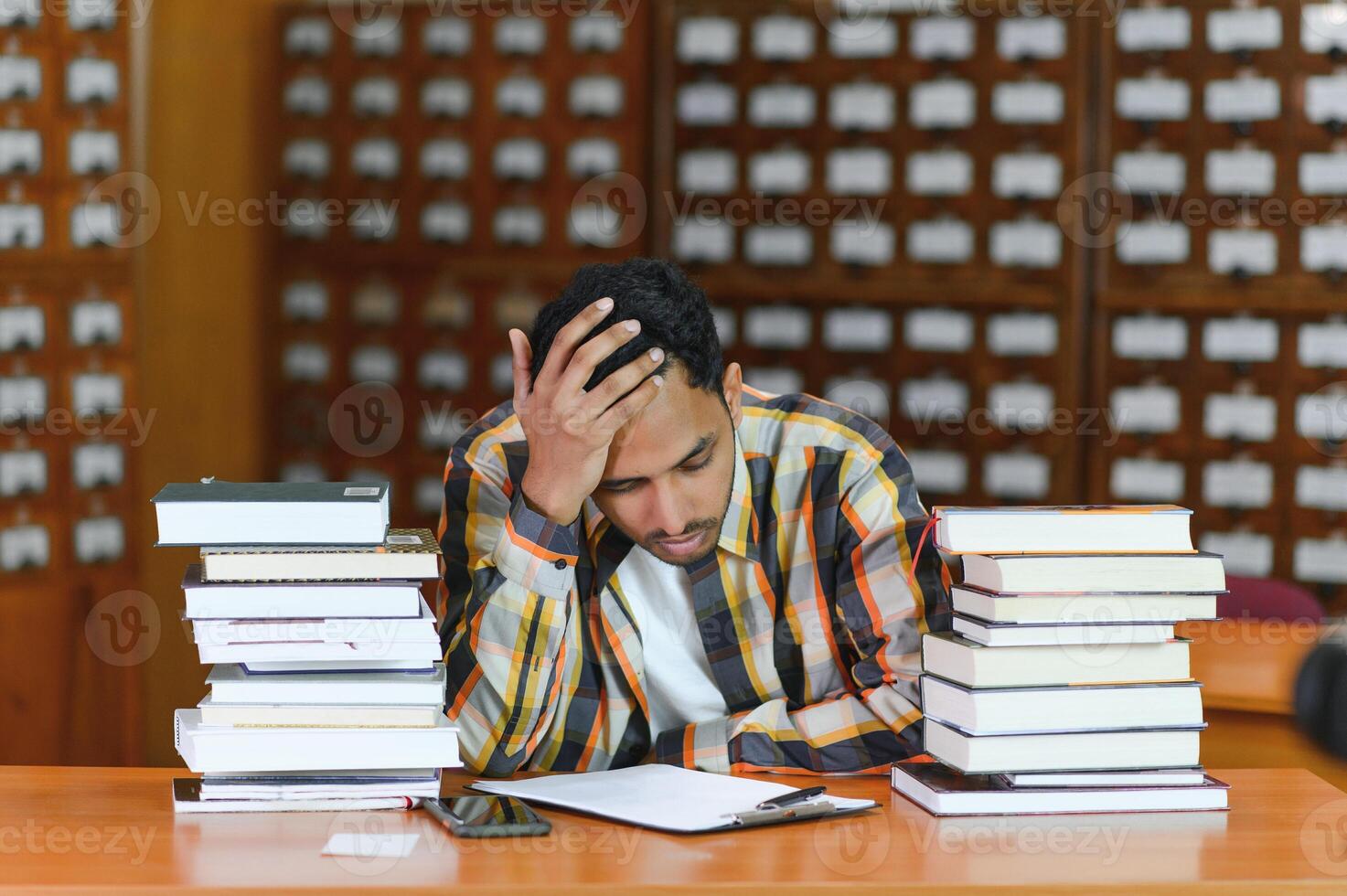 Portrait of cheerful male international Indian student with backpack, learning accessories standing near bookshelves at university library or book store during break between lessons. Education concept photo