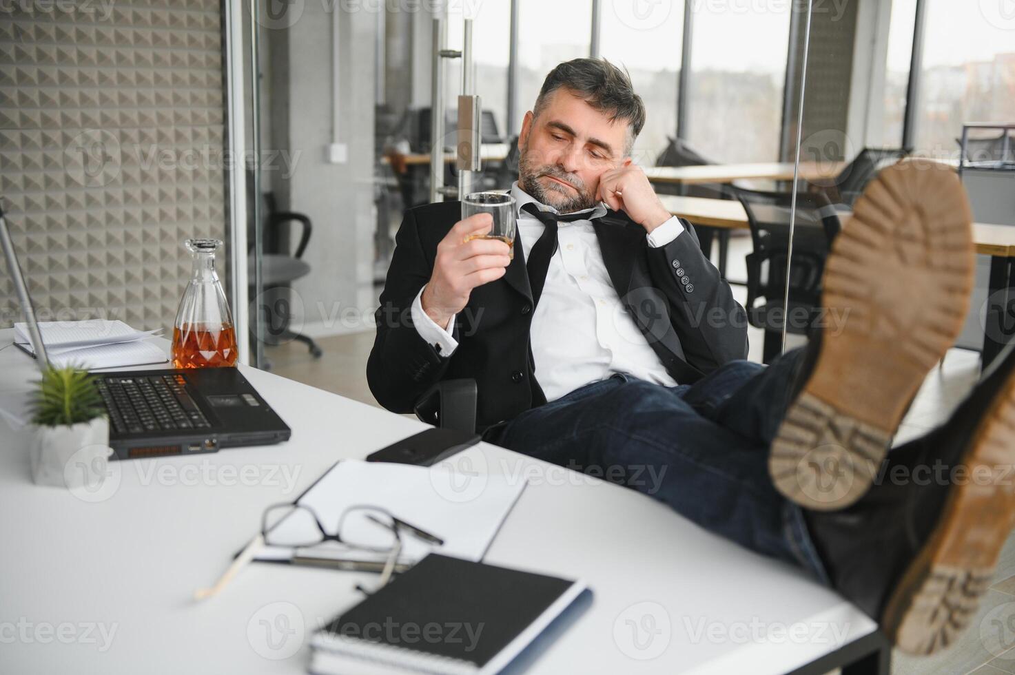 Old male employee drinking alcohol at workplace photo