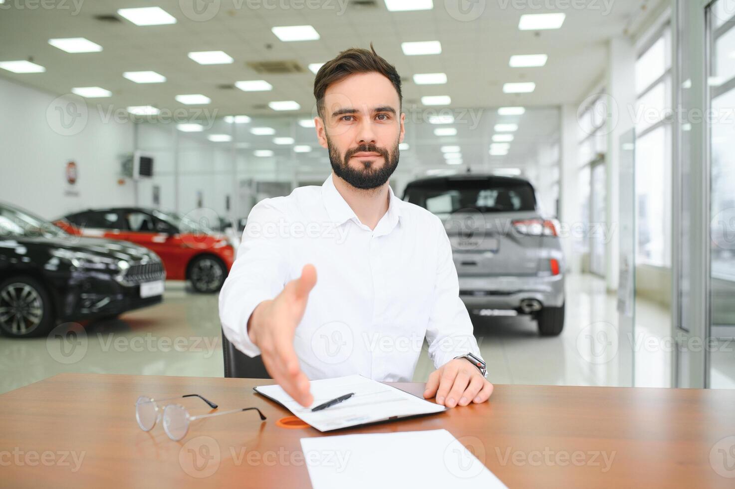 Smiling, friendly car seller standing in car salon. photo