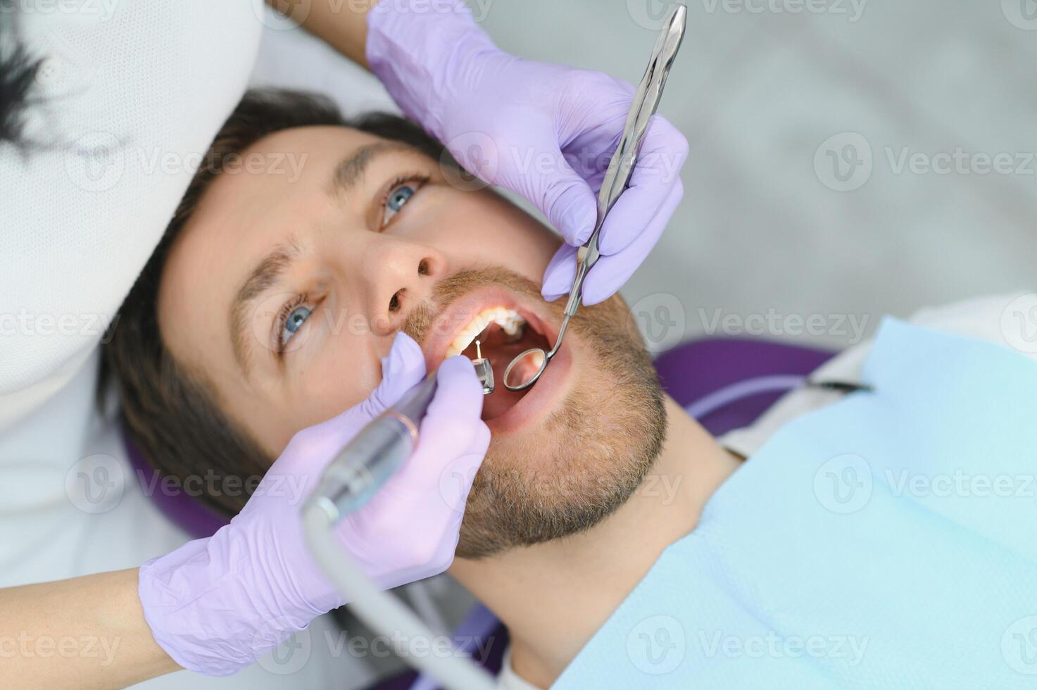 periodontal servicios. de cerca Disparo de sonriente hombre consiguiendo tratamiento en estomatológico clínica, dentista médico en guantes utilizando estéril dental herramientas para examinando dientes de masculino paciente foto