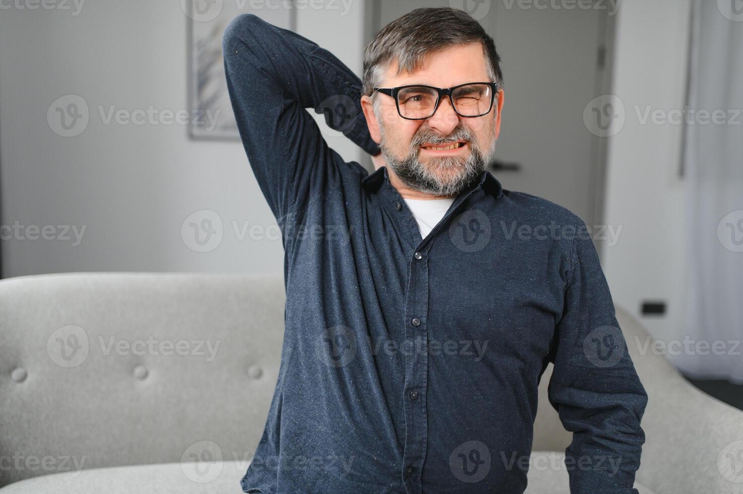 Neck Pain. Portrait Of Exhausted Mature Man Massaging Aching Neck Suffering From Ache Sitting On Couch At Home In Living Room. Osteoarthritis, Older People Health Problem, Sedentary Lifestyle Concept photo