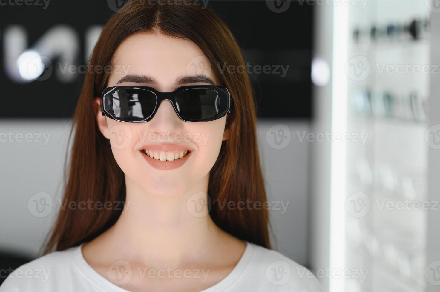 ella hecho su elección. hermosa joven mujer ajustando su nuevo Gafas de sol y sonriente mientras en pie en óptico almacenar. foto