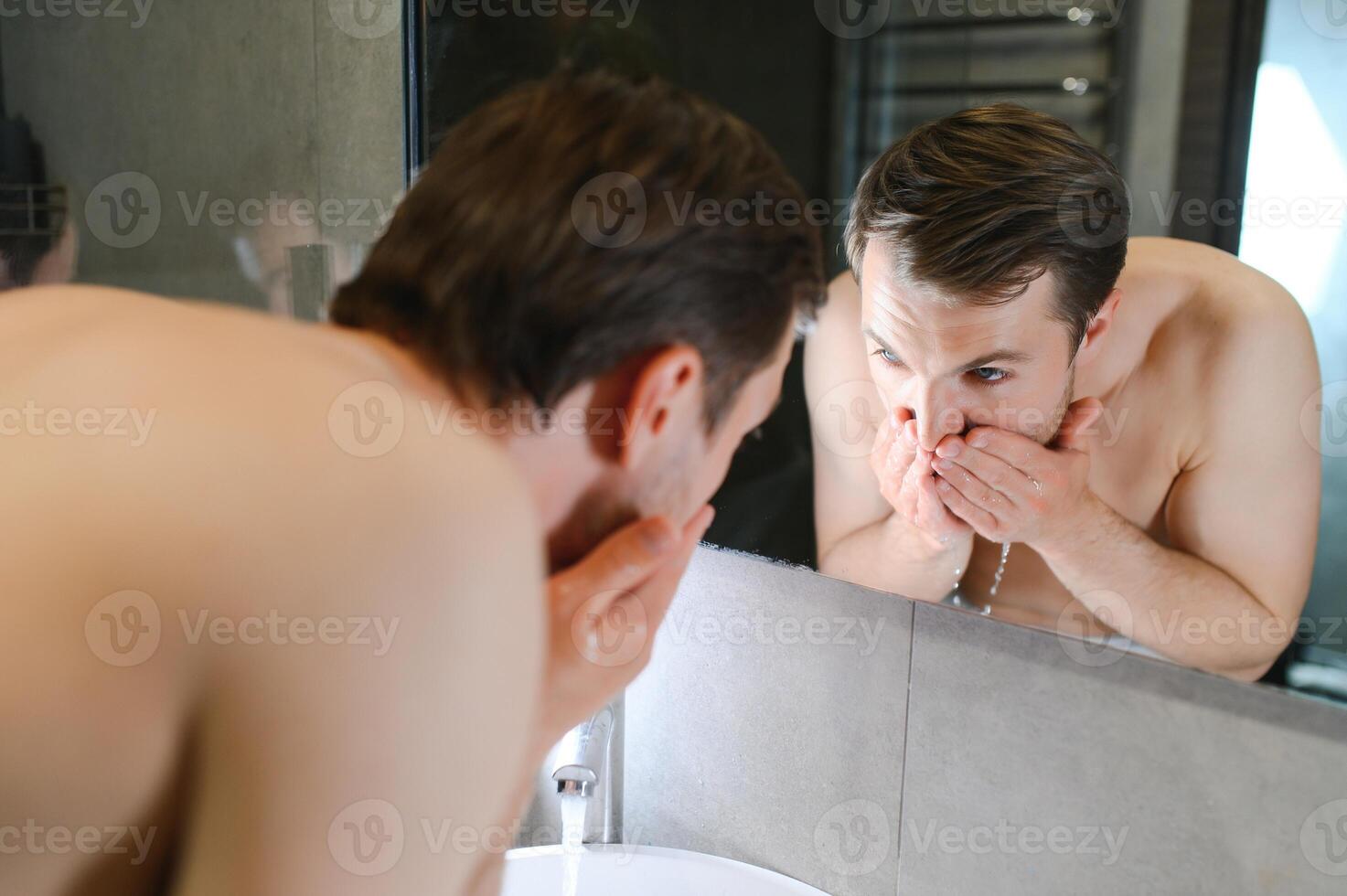 Bright caucasian man spraying water on his face after shaving in the bathroom at home photo