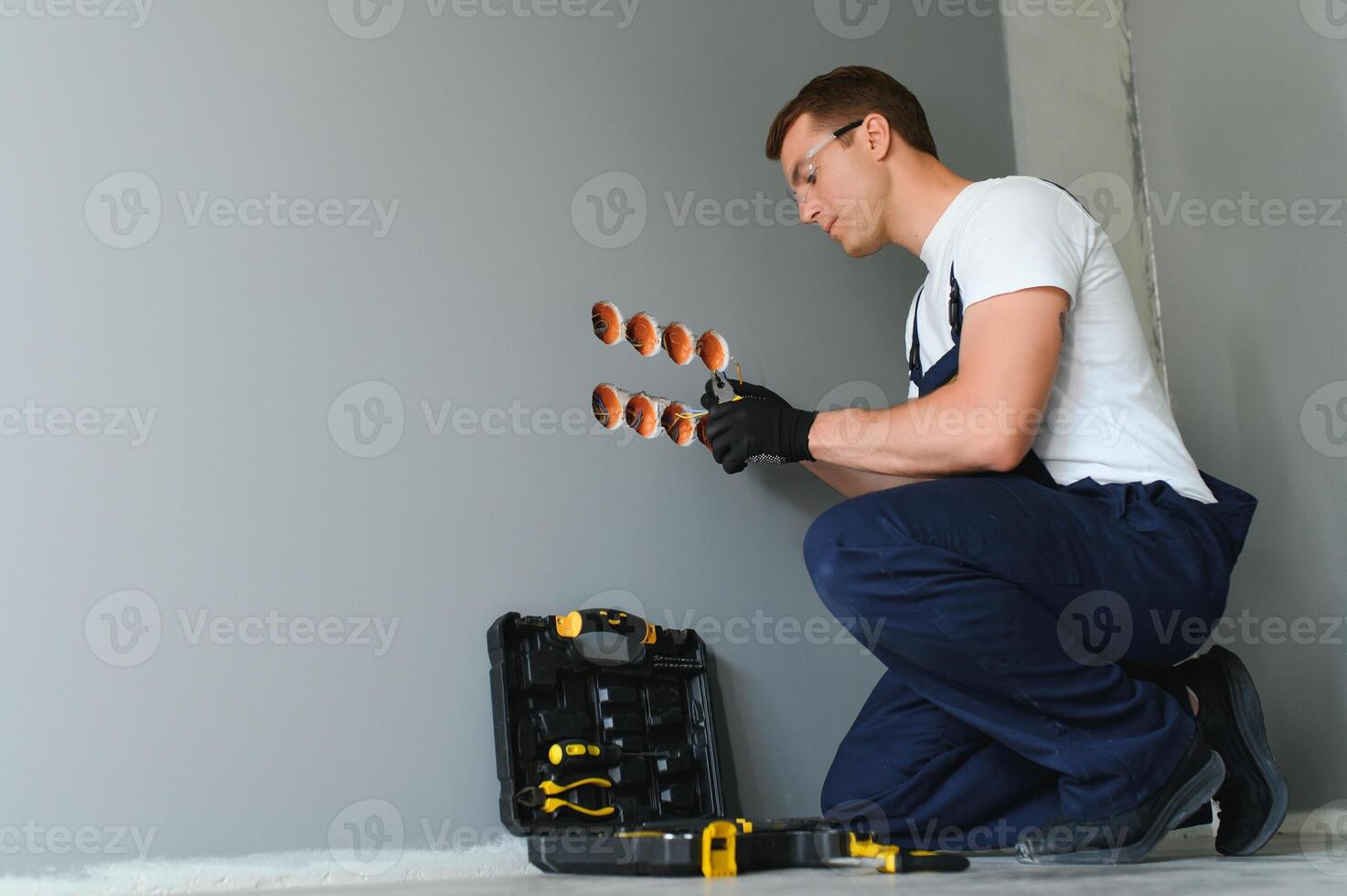 Electrician with screwdriver repairing power socket in room photo