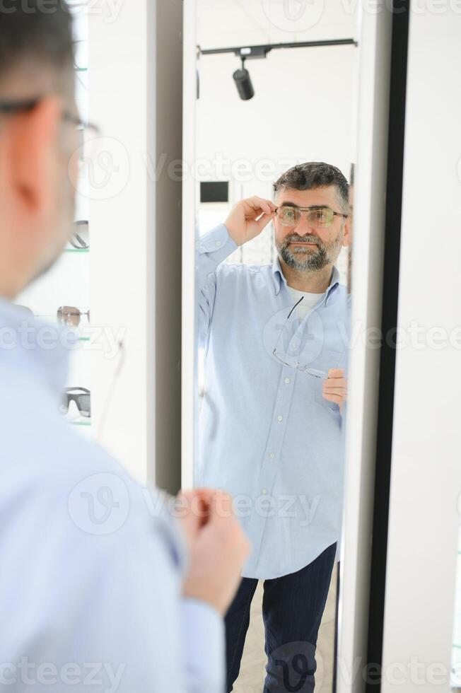 senior man choosing glasses in optic store. photo