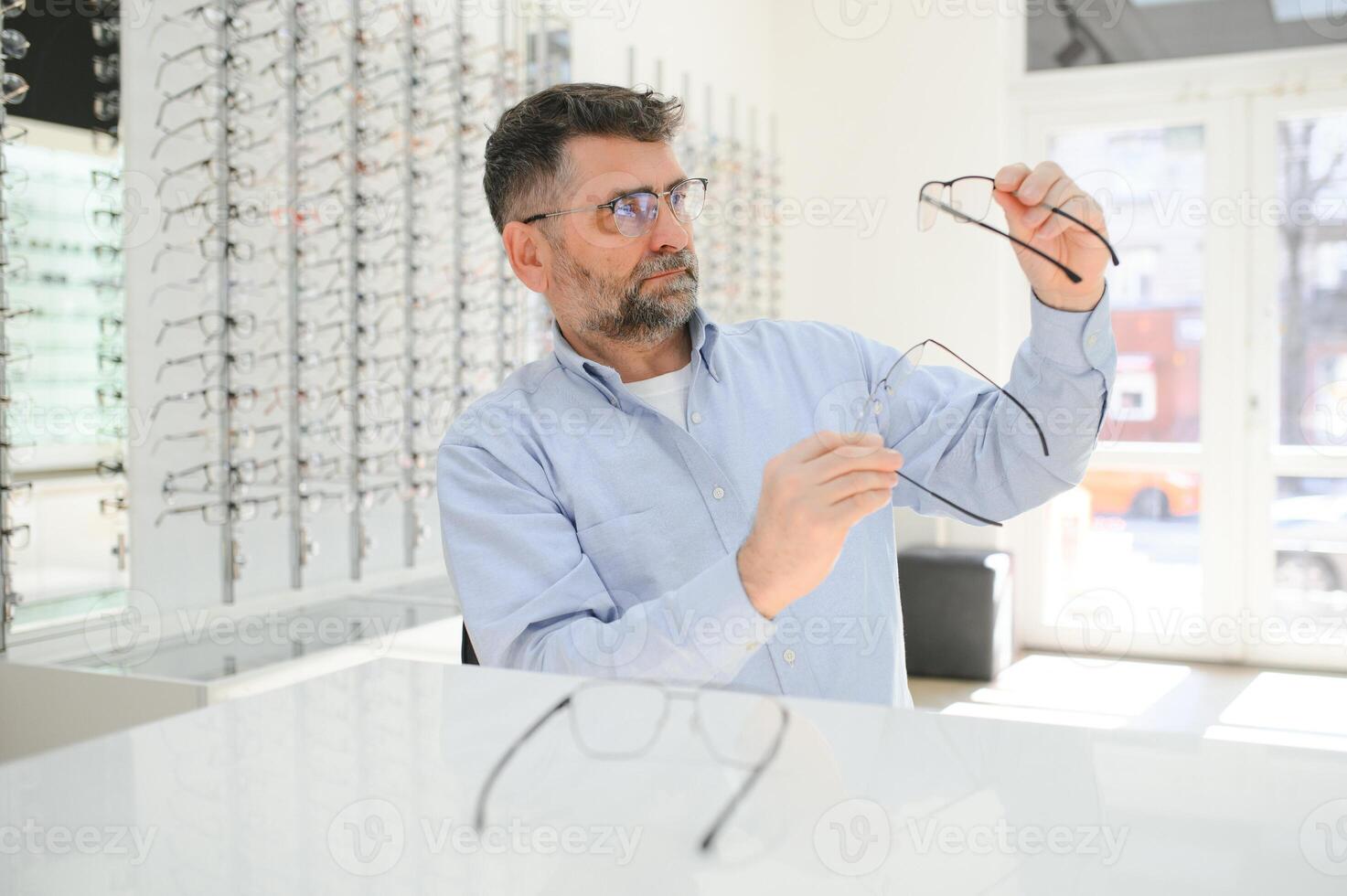 Handsome senior man choosing eyeglasses frame in optical store. photo