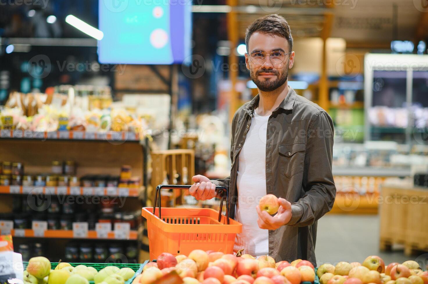 hermoso hombre compras en supermercado, sonriendo, utilizando teléfono. foto