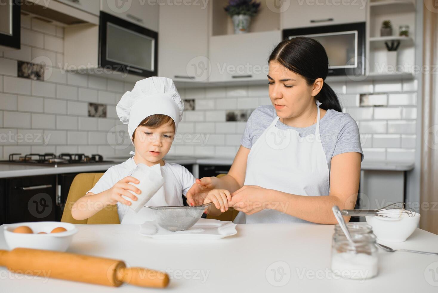 A young and beautiful mother is preparing food at home in the kitchen, along with her little son photo