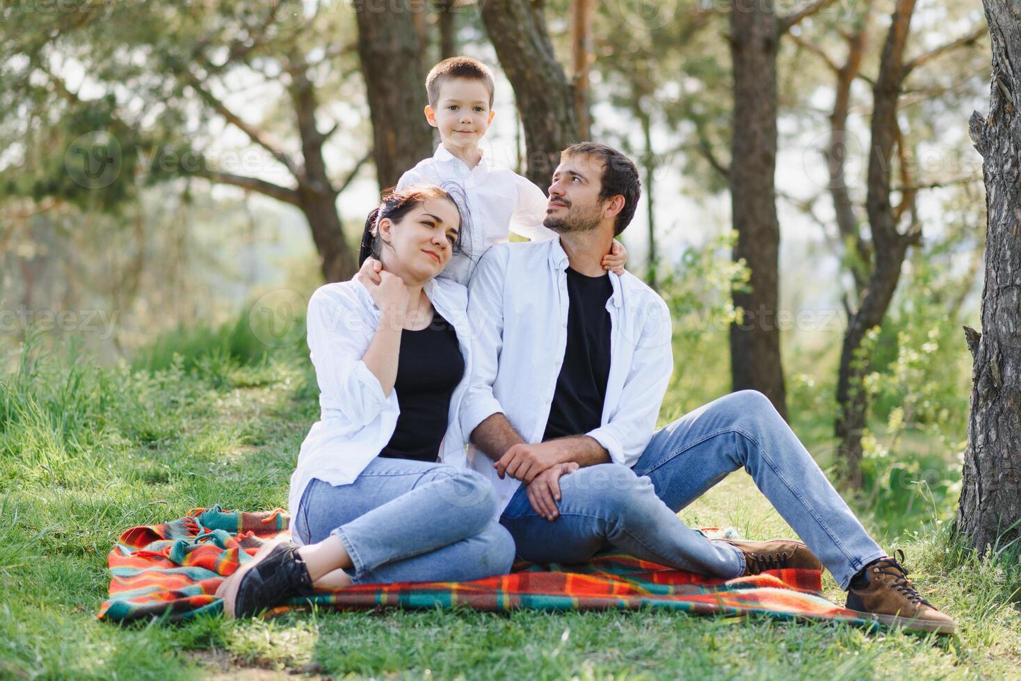 contento joven familia gasto hora al aire libre en un verano día tener divertido a hermosa parque en naturaleza mientras sentado en el verde césped. contento familia. foto