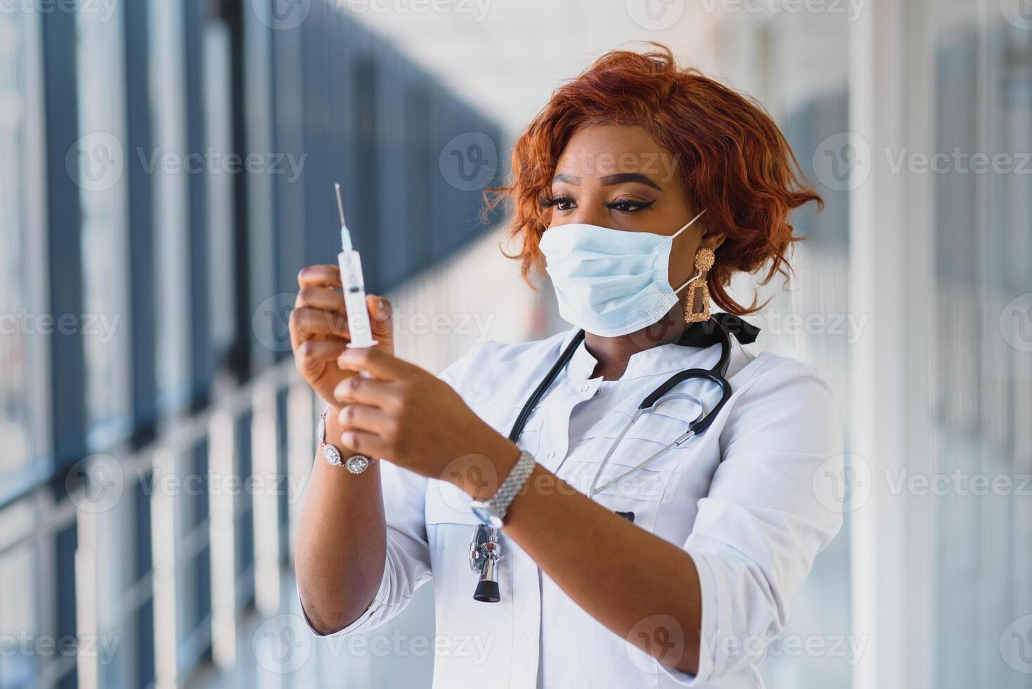 Young smiling African American doctor in medical mask holding a syringe photo