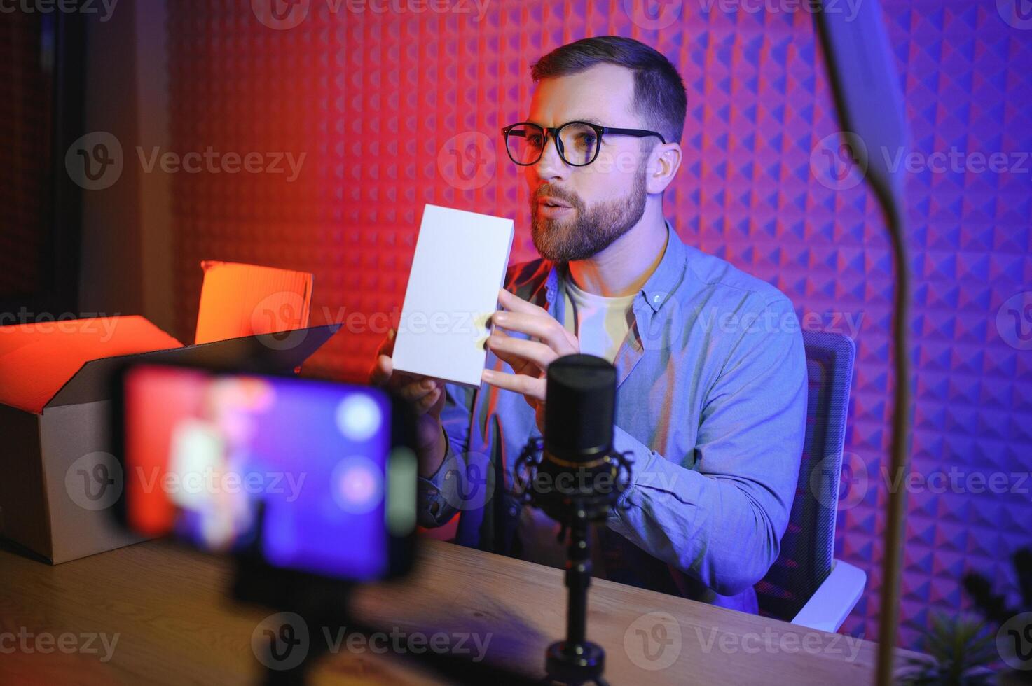 Joyful young man recording unboxing video in studio photo