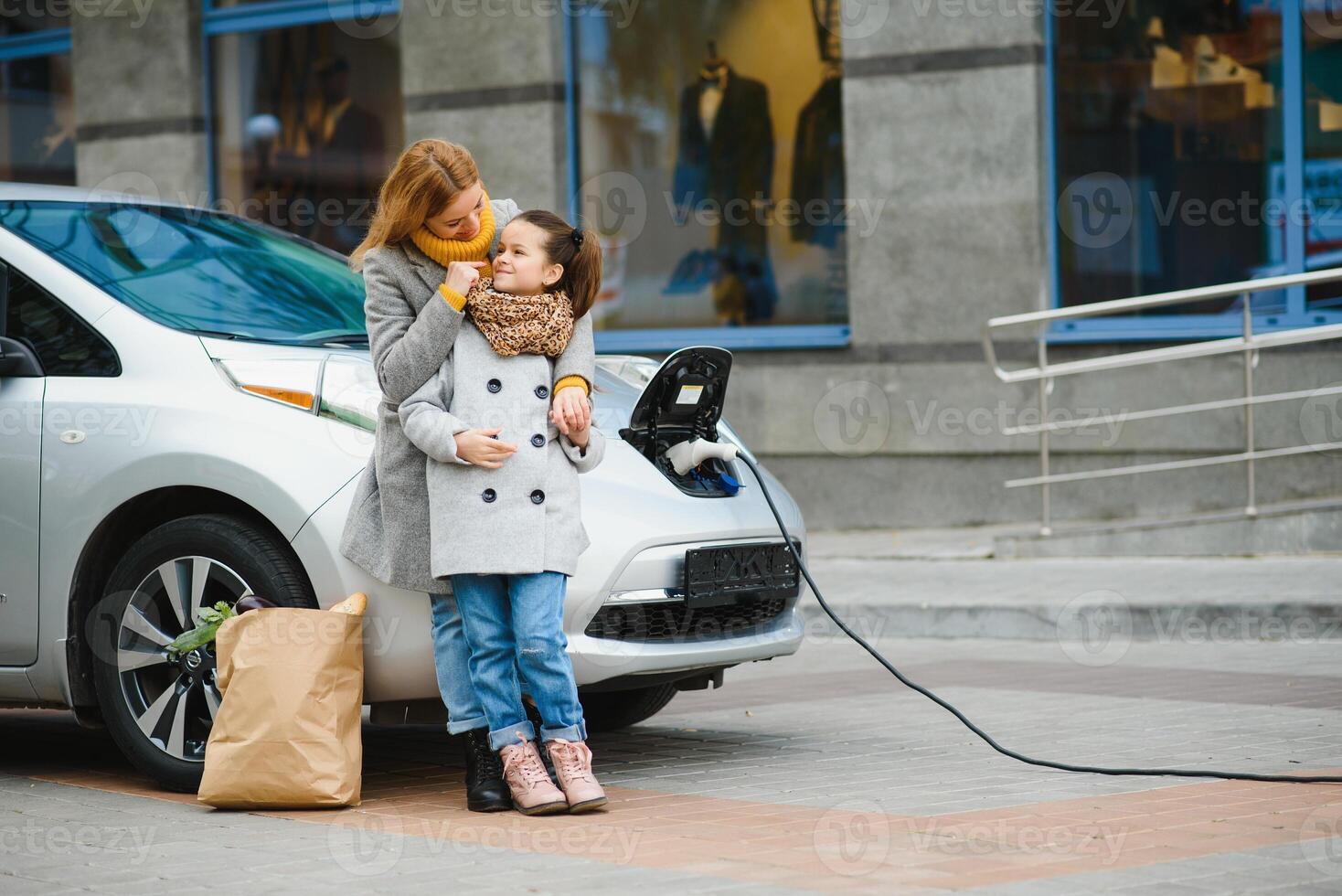 Stylish mother and daughter charge an electric car, and spend time together. photo