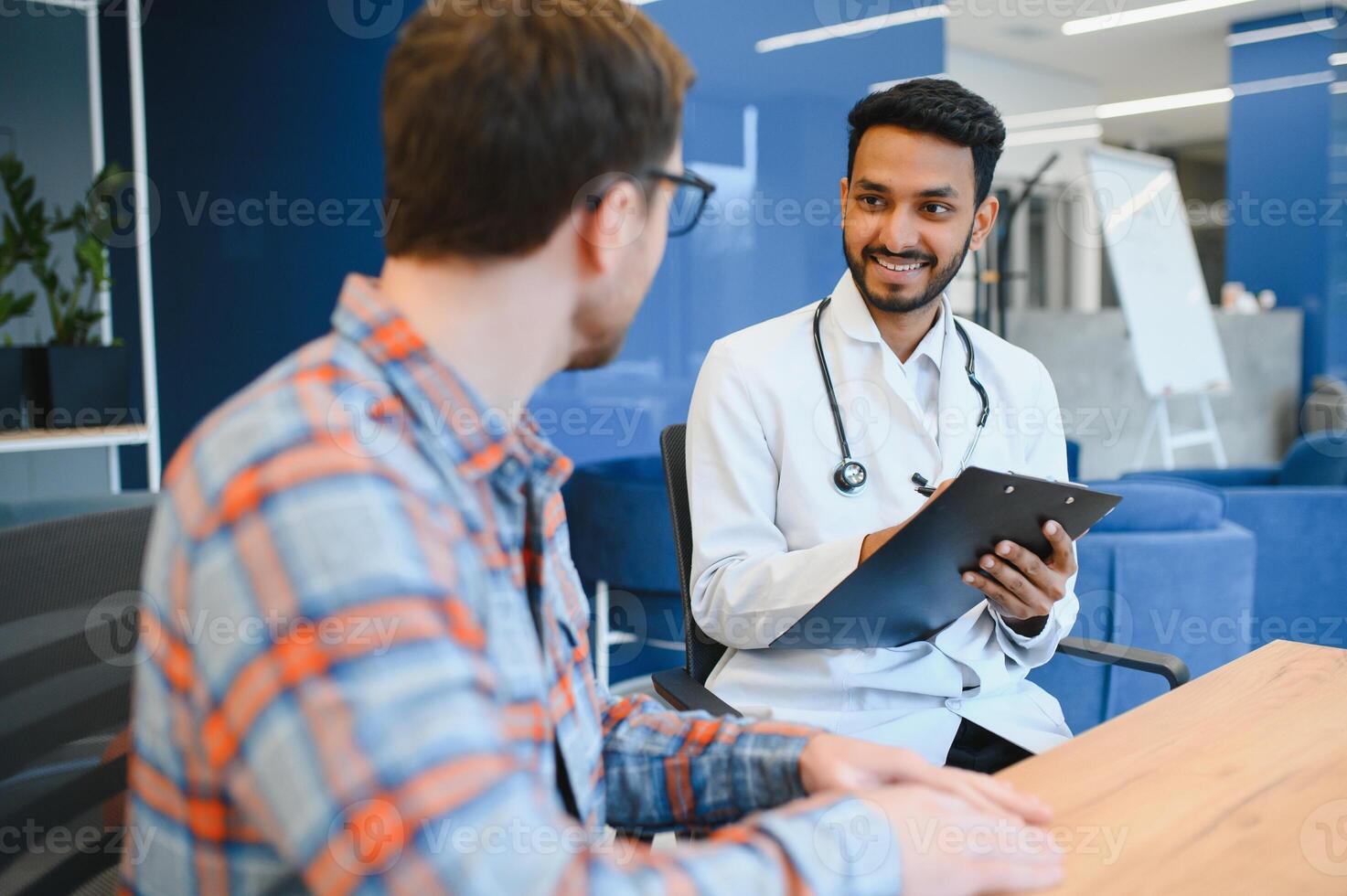 Indian doctor in white gown seeing patients in office. photo