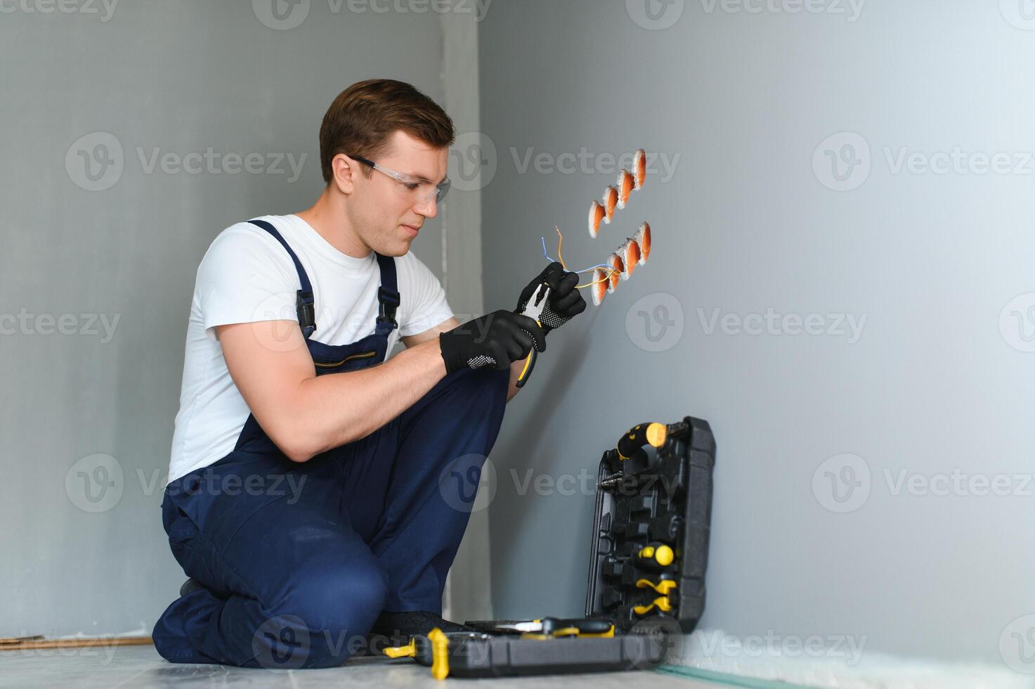 electricista técnico con guantes y la seguridad instrumentos arregla el eléctrico cable a el enchufe de un residencial instalación. foto