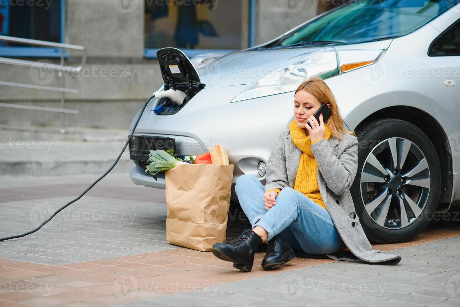 Using smartphone while waiting. Woman on the electric cars charge station at daytime. Brand new vehicle photo