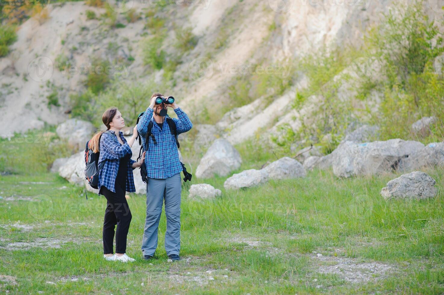 Couple of Young Happy Travelers Hiking with Backpacks on the Beautiful Rocky Trail at Warm Sunny Evening. Family Travel and Adventure Concept. photo