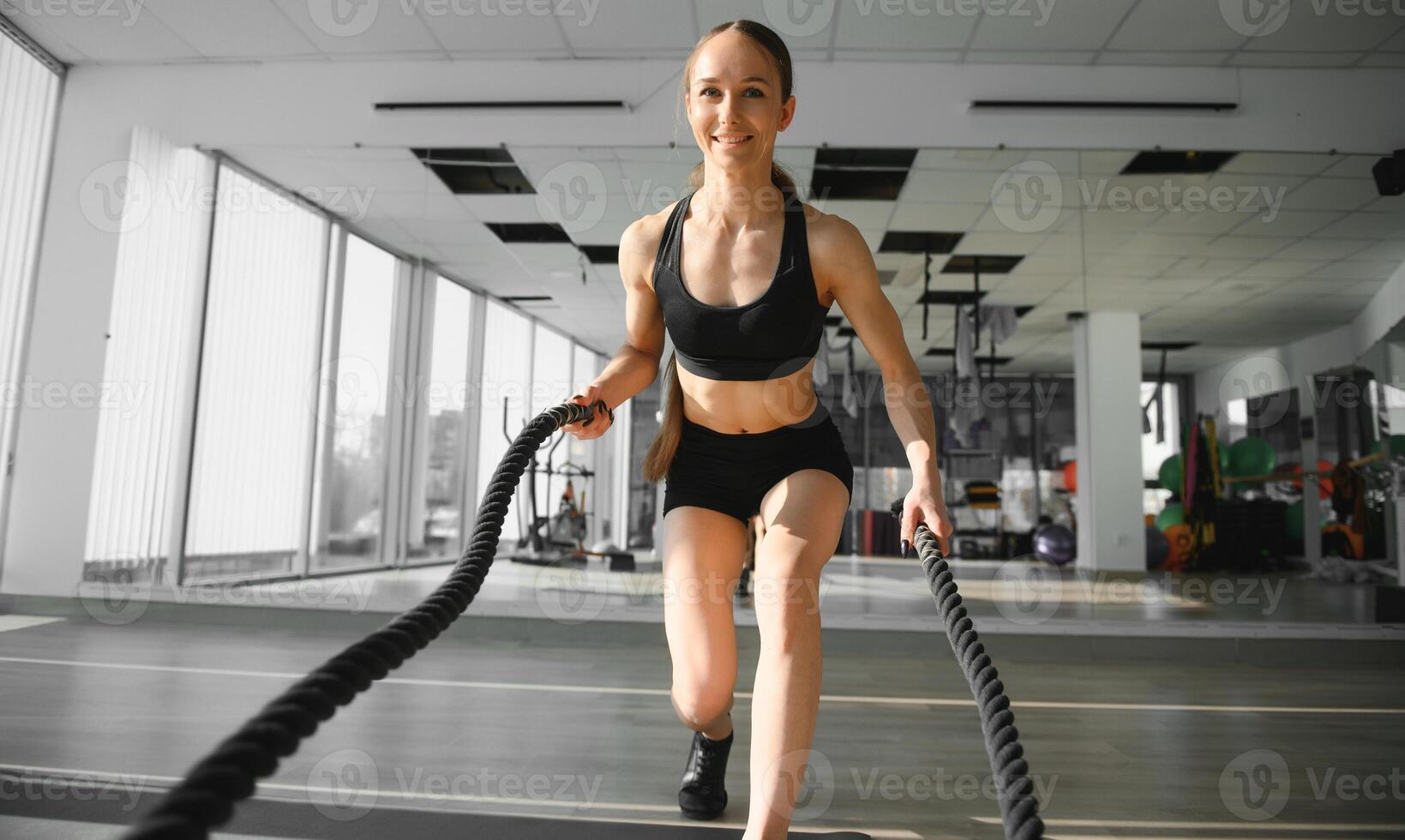 Athletic Female in a Gym Exercises with Battle Ropes During Her Fitness Workout High-Intensity Interval Training. She's Muscular and Sweaty photo