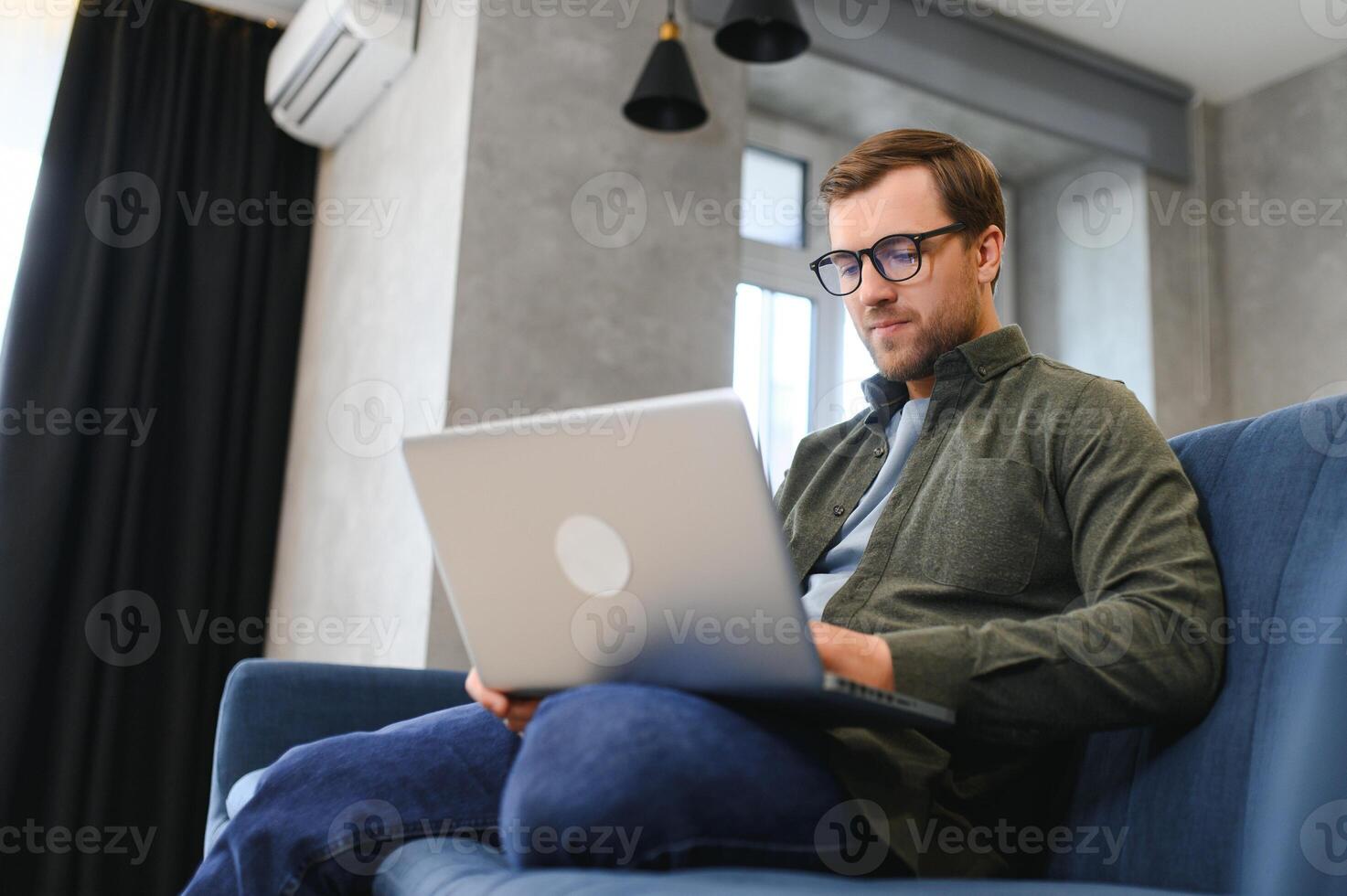 hombres trabajando en ordenador portátil computadora en su habitación. hogar trabajo o estudiar, Lanza libre concepto. joven hombre sentado relajado en sofá con ordenador portátil. moderno empresario utilizando ordenador portátil. foto