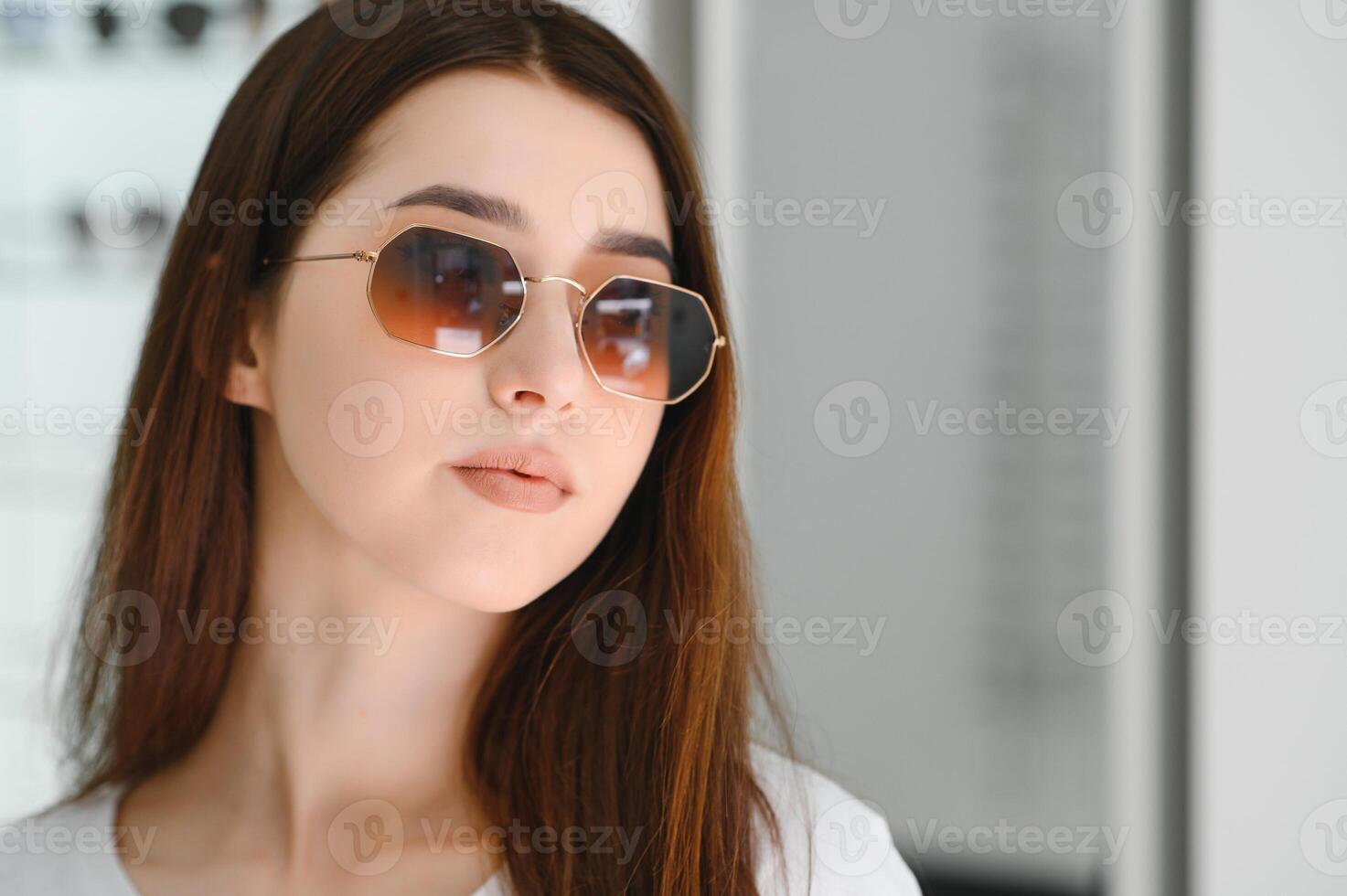 ella hecho su elección. hermosa joven mujer ajustando su nuevo Gafas de sol y sonriente mientras en pie en óptico almacenar. foto