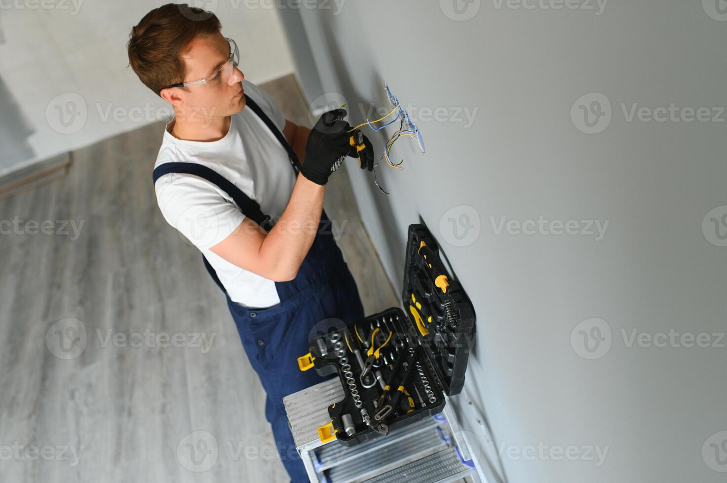 electricista técnico con guantes y la seguridad instrumentos arregla el eléctrico cable a el enchufe de un residencial instalación. foto