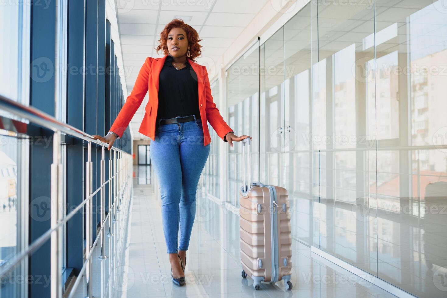 Full length side portrait of young black woman walking with suitcase in airport photo