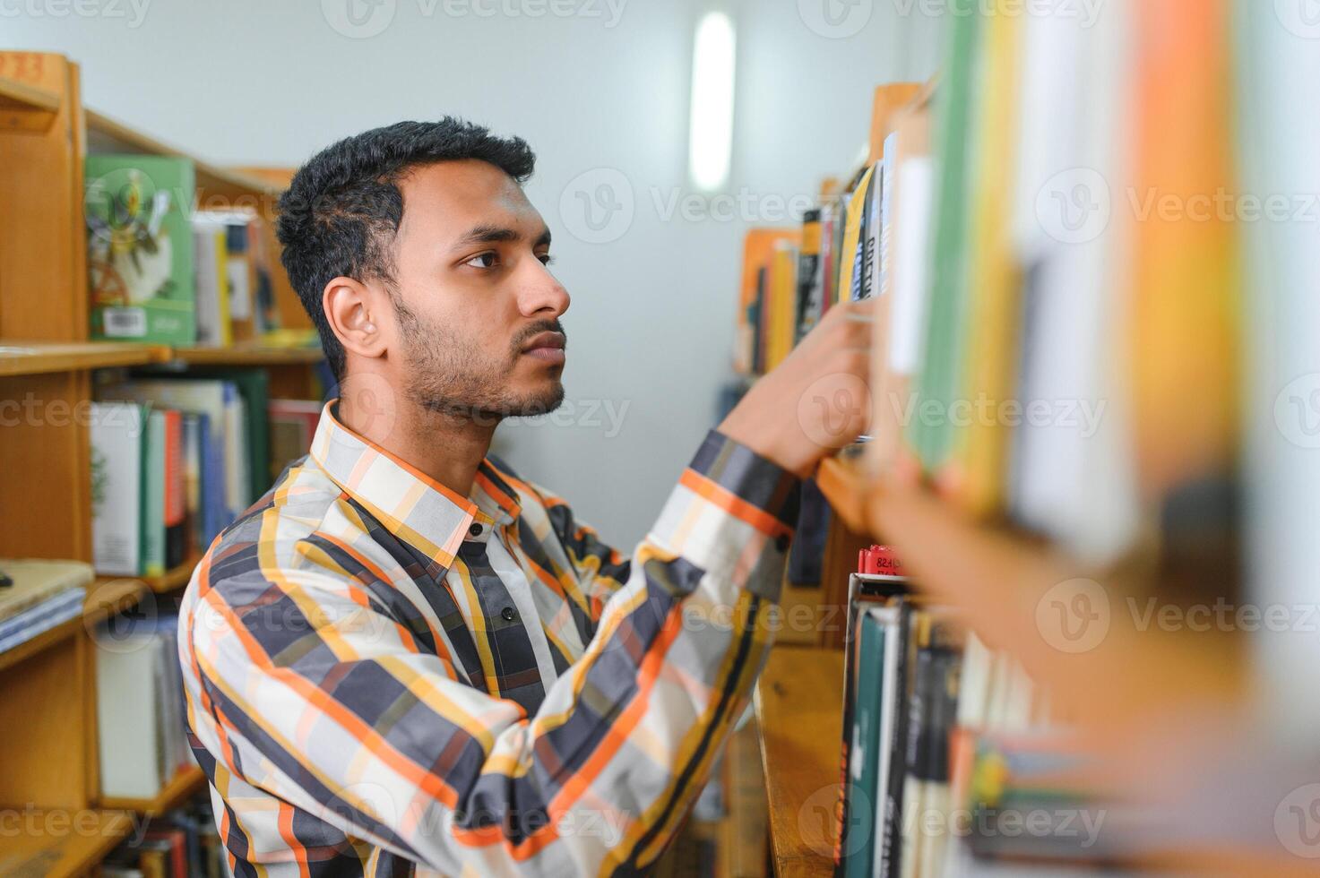 masculino indio estudiante a el biblioteca con libro foto