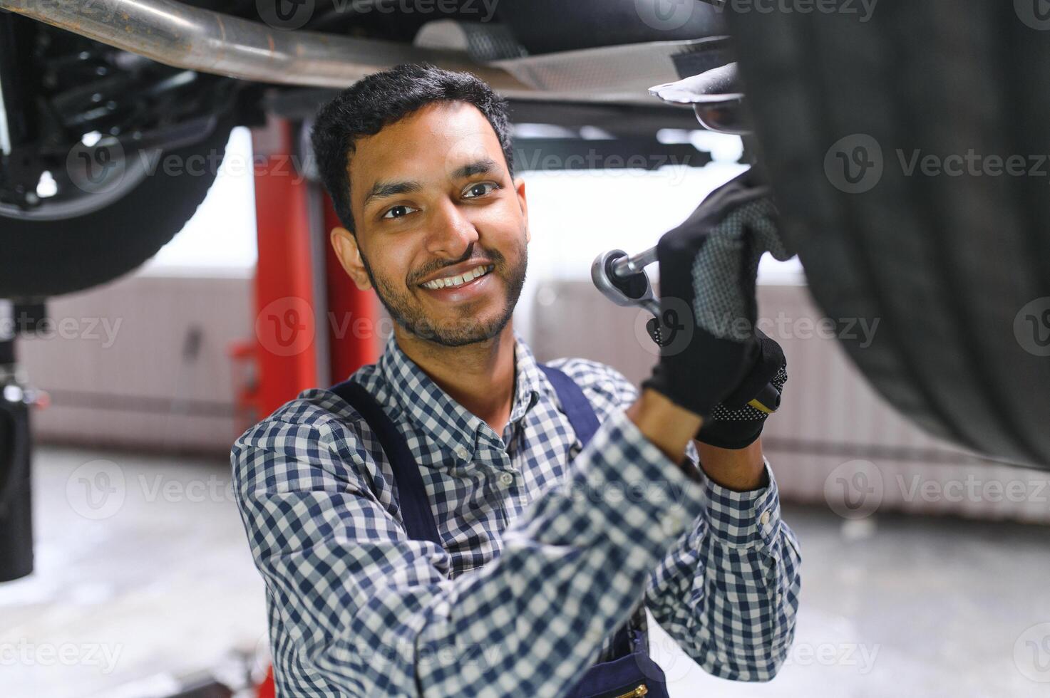 latín Hispano auto mecánico en uniforme es examinando un coche mientras trabajando en auto Servicio foto