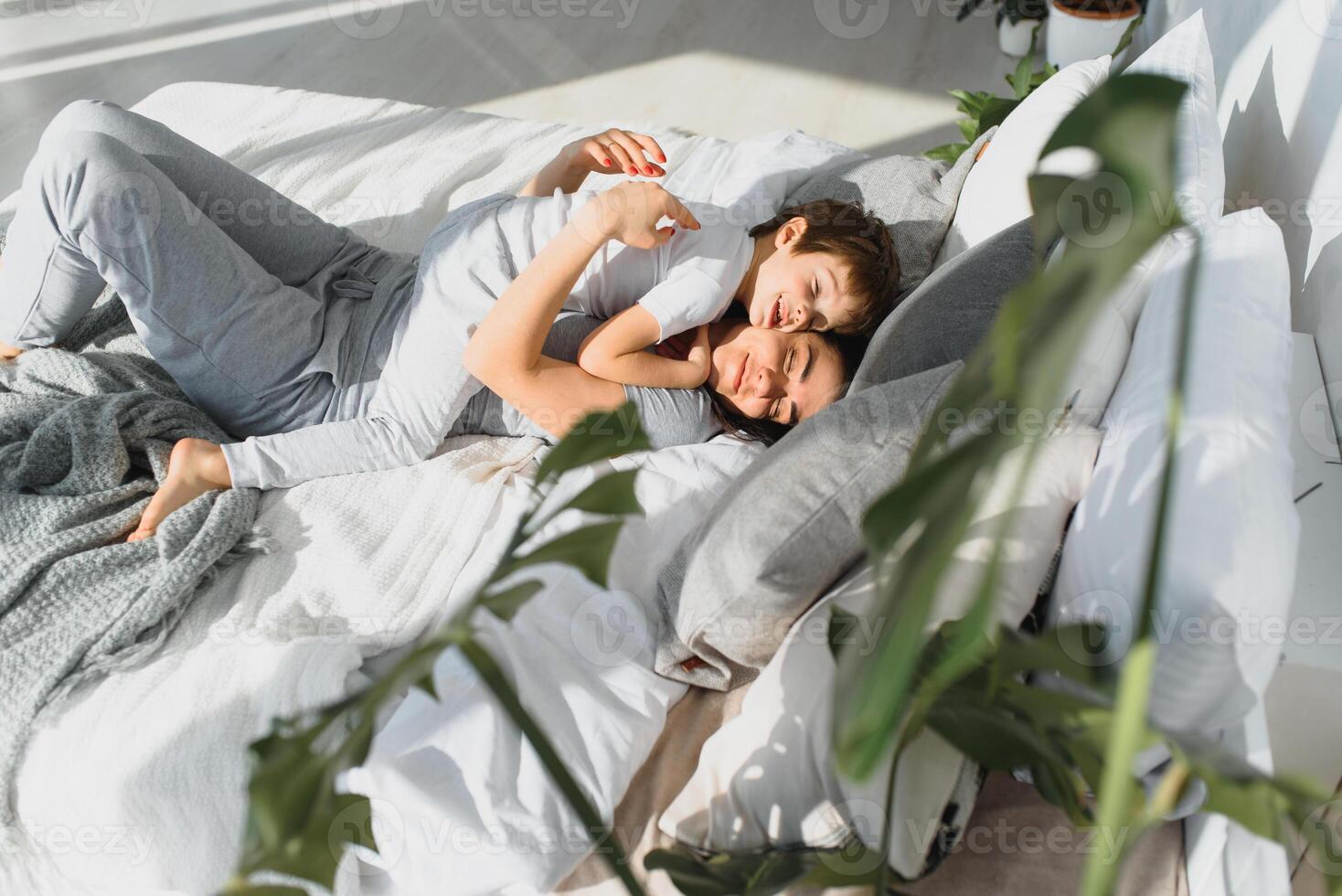 Young mother with her 5 years old little son dressed in pajamas are relaxing and playing in the bed at the weekend together, lazy morning, warm and cozy scene. Family home shoot. photo