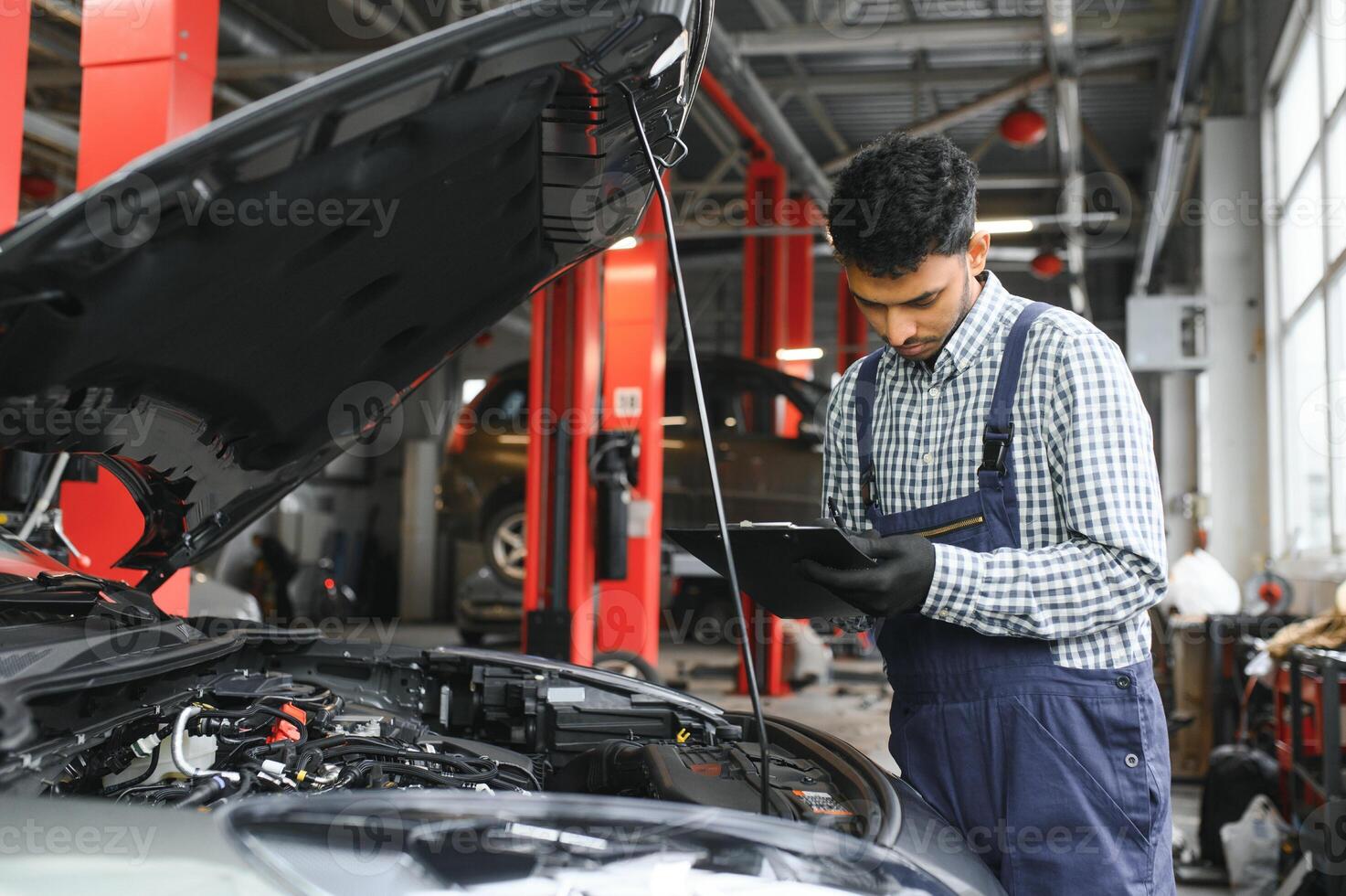 latín Hispano auto mecánico en uniforme es examinando un coche mientras trabajando en auto Servicio foto