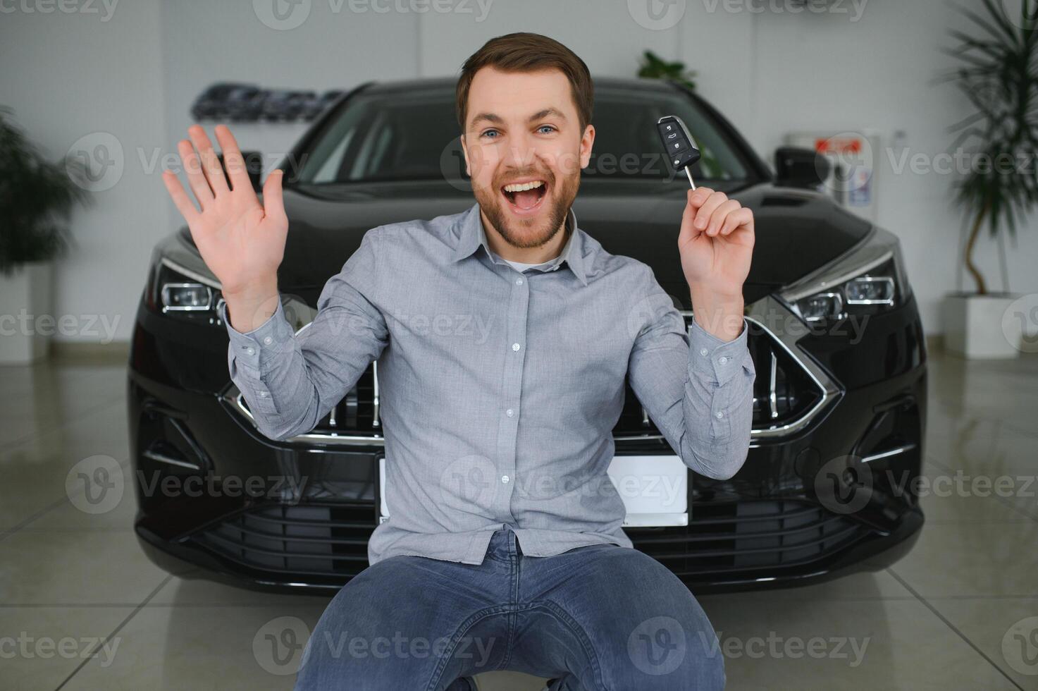 Emotional handsome guy raising hand up and smiling at camera. Rich man buying auto at luxury dealership salon photo