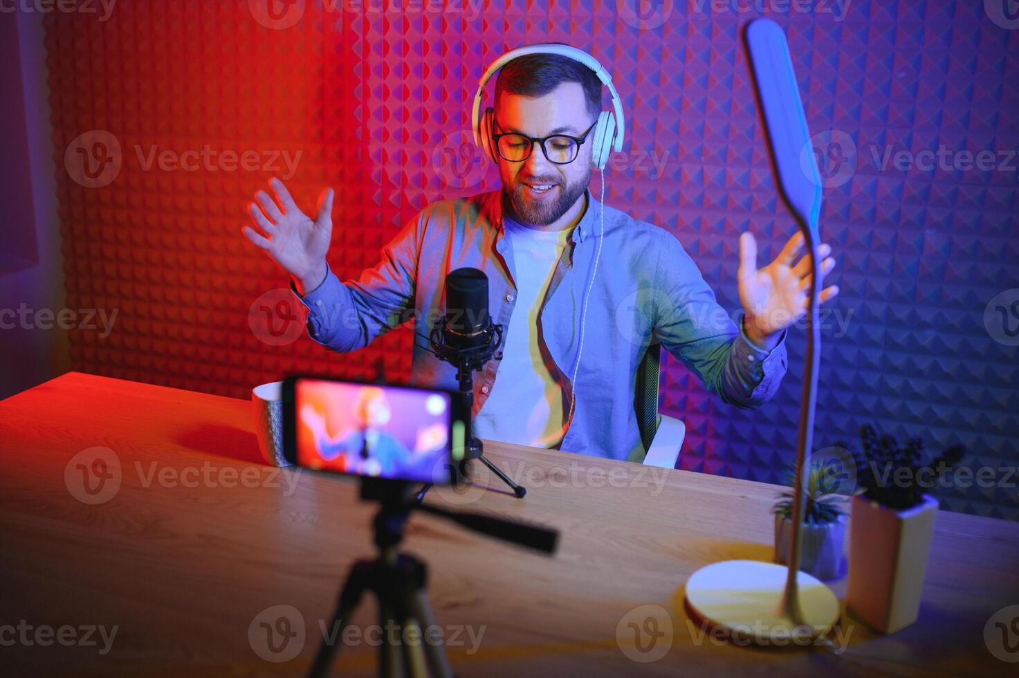 vlogger utilizando teléfono inteligente a película podcast en estudio. blogger con móvil teléfono, micrófono y auriculares rodaje vídeo para social medios de comunicación radiodifusión carrera profesional. foto