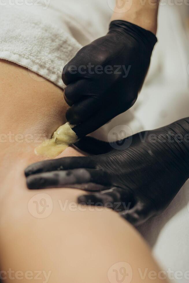 Woman cosmetologist doing sugaring hair removal under armpit photo