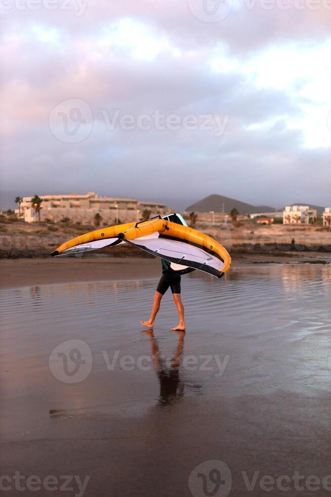 a man walks along the ocean beach with WING FOIL photo