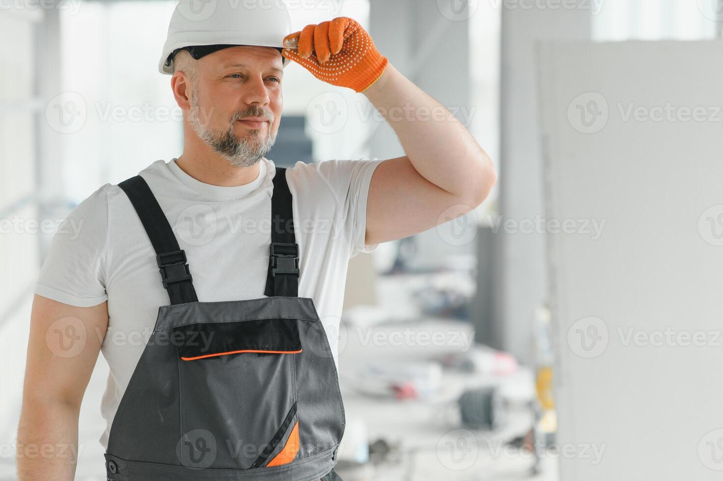 Portrait of a builder in working uniform with protective helmet standing with instruments at the construction site indoors photo