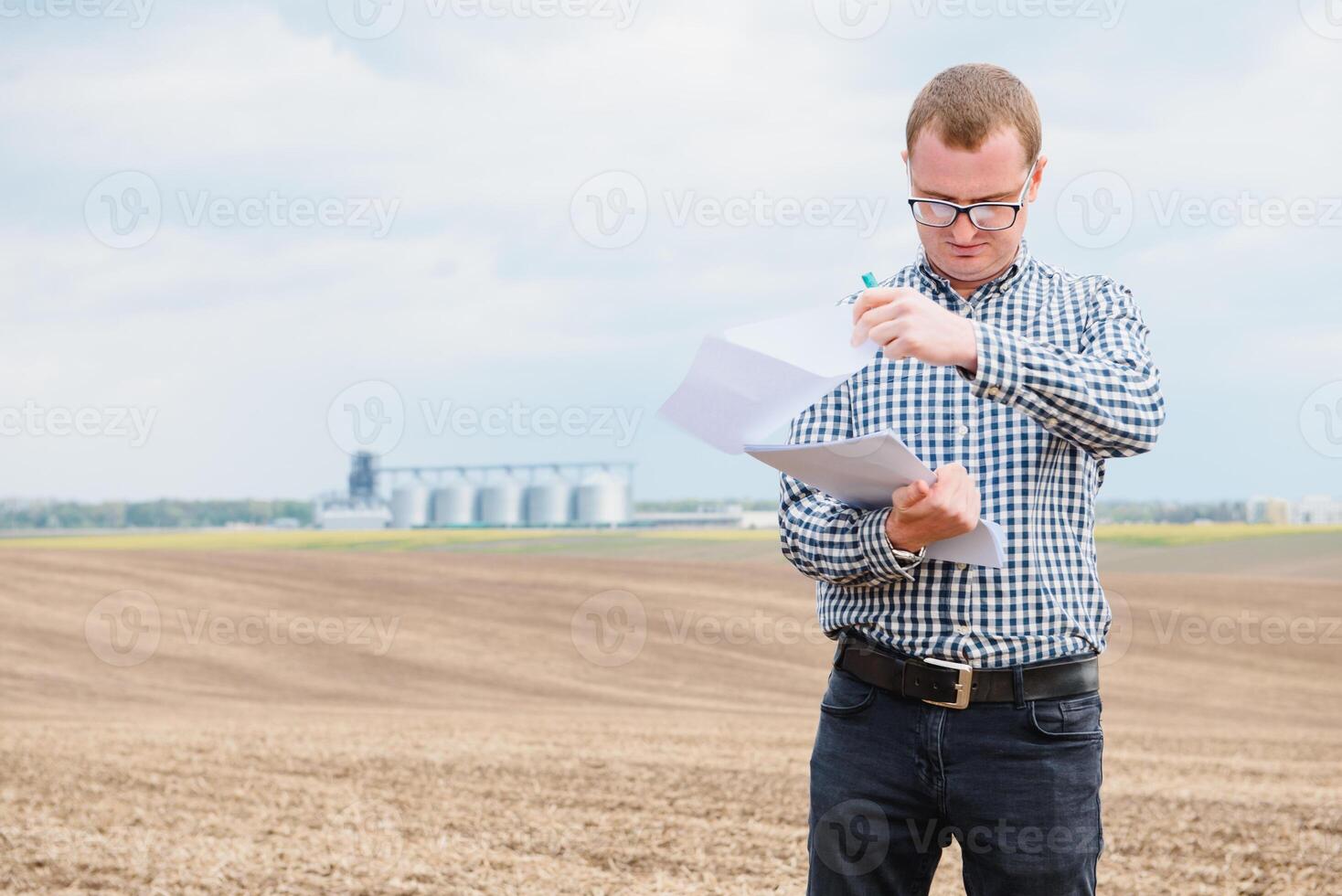 Happy farmer with laptop standing in wheat field in front of grain silo photo