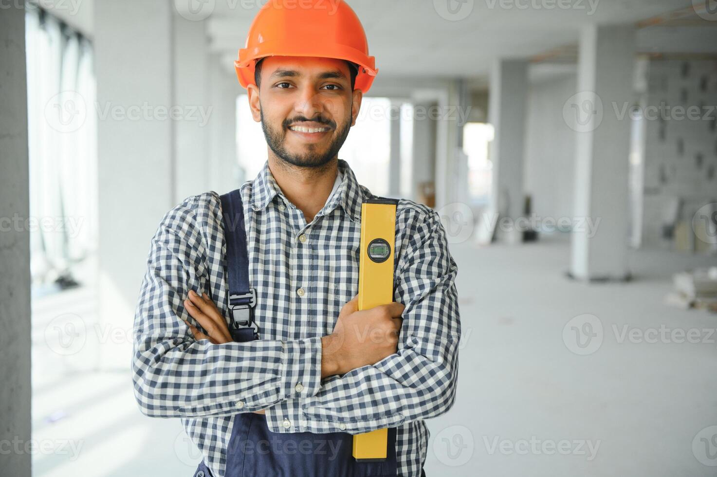 Indian construction site manager standing wearing helmet, thinking at construction site. Portrait of mixed race manual worker or architect. photo
