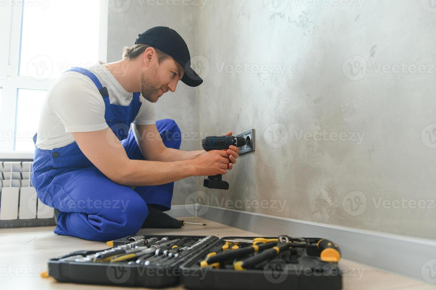 Confident professional electrician in uniform using screwdriver while replacing a socket in apartment after renovation work photo