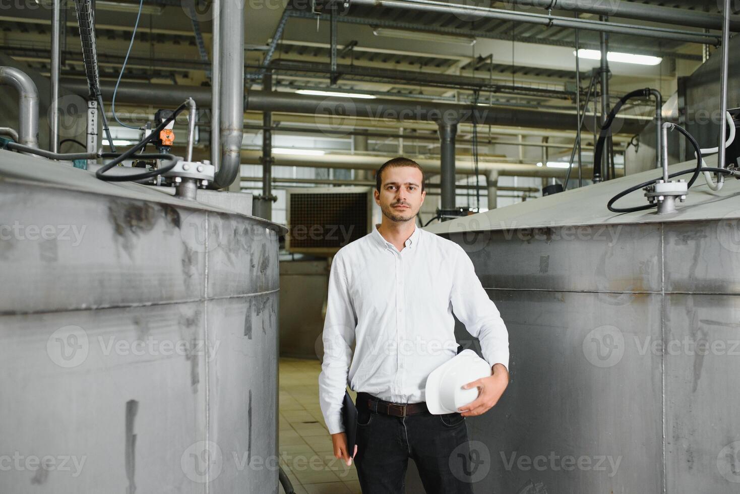 Smiling and happy employee. Industrial worker indoors in factory. Young technician with white hard hat. photo