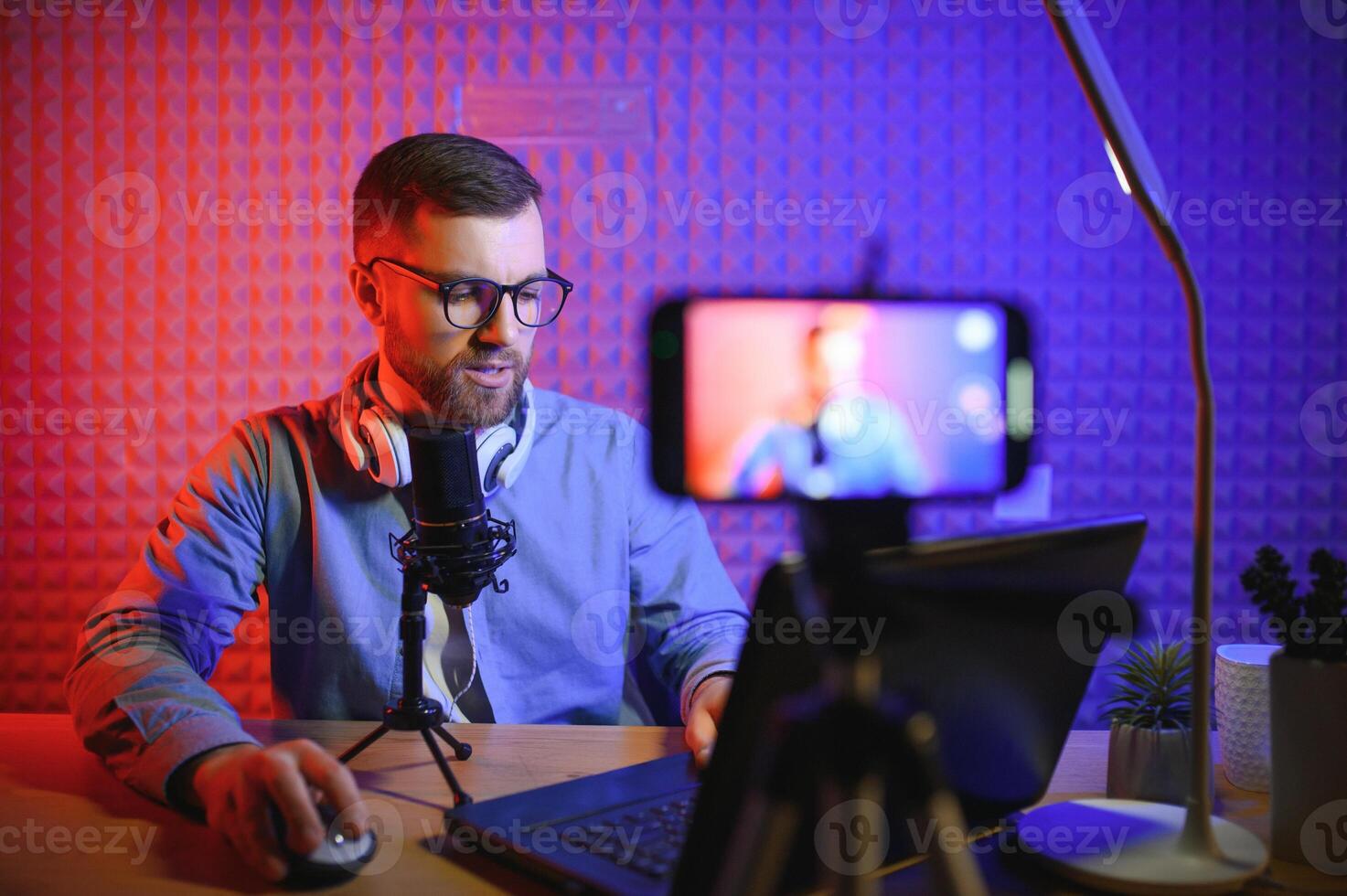 vlogger using smartphone to film podcast in studio. blogger with mobile phone, microphone and headphones filming video for social media broadcasting career. photo