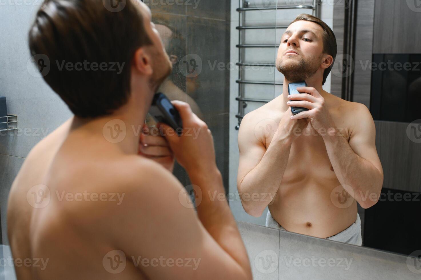 Handsome young bearded man trimming his beard with a trimmer. photo